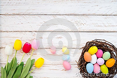 Colorful Easter eggs in nest with tulip flower on rustic wooden planks background. Stock Photo