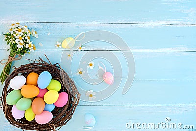 Colorful Easter eggs in nest with wildflowers on on rustic wooden planks background in blue paint. Stock Photo