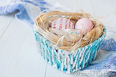 Colorful Easter Eggs on the white rustic wooden background with nest and blue basket on the linen towel Selective focus. Stock Photo