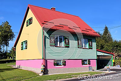 Colorful family house with metal roof and decorated wooden window blinds surrounded with garden elves and other garden decoration Stock Photo