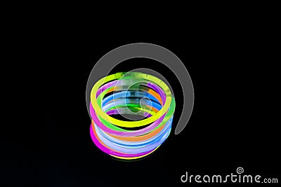 Colorful fluorescent light neon glow stick bracelet strap wristband on mirror reflection black background Stock Photo
