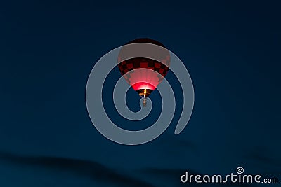 Colorful hot air balloon in dark pink and purple colors glowing in a dark blue early morning sky Stock Photo