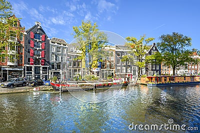 Colorful houseboats line the canal in front of colorful Dutch homes on a sunny day in early autumn in Amsterdam, Netherlands Editorial Stock Photo