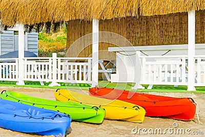Colorful kayaks on white sand on the beach of Cyprus against summer house with white wooden fence and reed roof Stock Photo