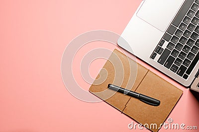 Colorful layout composition with a grey laptop with a black keyboard, brown notepad, and a pen on a pastel pink background Stock Photo