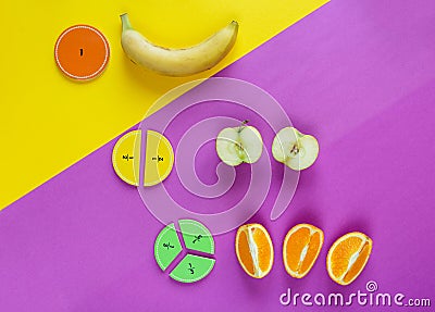 Colorful math fractions and apples, oranges, banana as a sample on yellow purple background. Interesting fun math for kids. Stock Photo