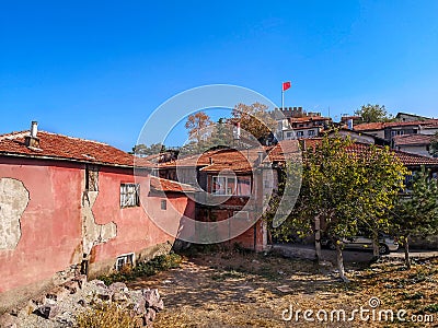 Colorful old houses with pink walls and a red tiled roof on the background of the tower of Ankara Castle with the Turkish flag. Stock Photo