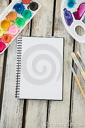 Colorful palette, paintbrushes and blank book on wooden surface Stock Photo