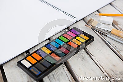 Colorful palette, paintbrushes and book on wooden surface Stock Photo