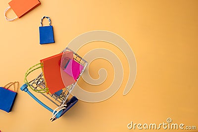 Colorful paper shopping bag and trolley go down from floating yellow background for copy space Stock Photo