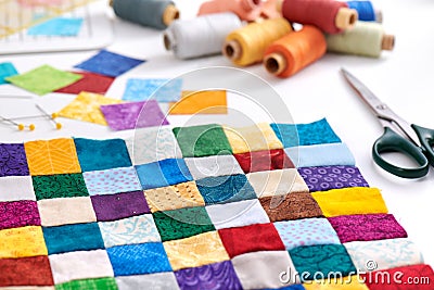 Colorful part of quilt sewn from square pieces, spools of thread, scissors, quilting and sewing accessories Stock Photo