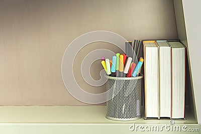 Colorful pen in metal pen pot and books on shelve Stock Photo