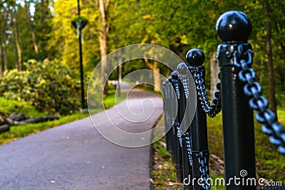 Colorful Photo of the Road in a Park, Between Woods - Closeup view of the Chain Fence with Blurred Background with Space for Text Stock Photo