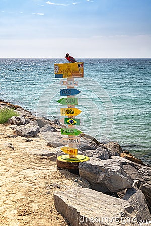 Colorful pole with arrows pointing to place names around the world, on the beach of San Remo Editorial Stock Photo