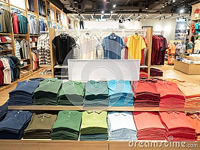 Colorful polo t shirt stack on shelf in large department store shop. Copy space on white sign board. Stock Photo