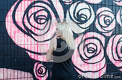 Colorful portrait of pretty young blond woman posing on graffiti wall background in black dress Editorial Stock Photo