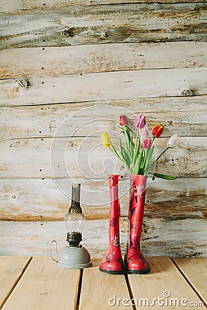 Colorful rain boots with spring flowers and oli lamp in wooden b Stock Photo