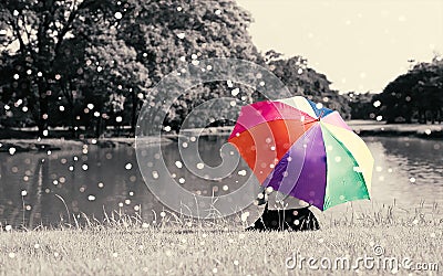 Colorful rainbow umbrella hold by sitting woman on grass field near river at outdoor with full of nature and rain, Relax concept, Stock Photo