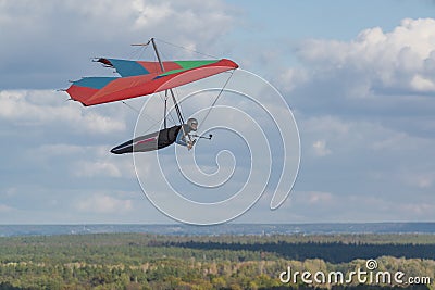 Colorful red hang glider wing soars over fields and forests Stock Photo