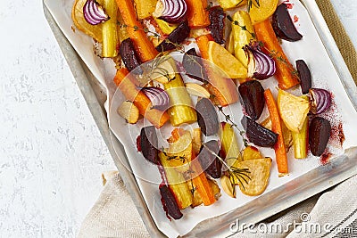 Colorful roasted vegetables on tray with parchment. Mix of carrots, beets, turnips, rutabaga, onions. Vegetarianism, veganism, Stock Photo