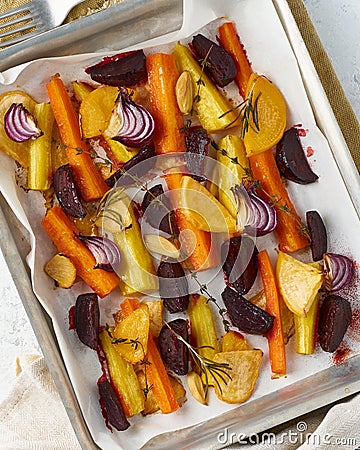 Colorful roasted vegetables on tray with parchment. Mix of carrots, beets, turnips, rutabaga, onions. Vegetarianism, veganism, Stock Photo