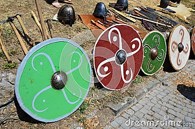 Colorful round shields, light batlle axes, conical helmets and various knives displayed on medieval summer festival Stock Photo