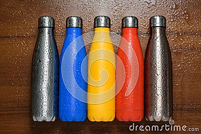 Colorful stainless thermos bottles on a wooden table sprayed with water. Stock Photo