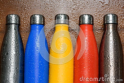 Colorful stainless thermos bottles on a wooden table sprayed with water. Stock Photo