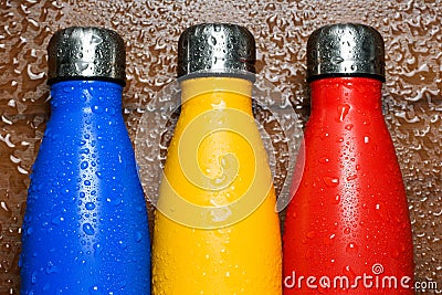 Colorful stainless thermos bottles on a wooden table sprayed with water. Stock Photo