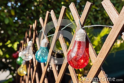 Colorful string bulbs hanging on a wooden fence in a back yard. Getting ready to party concept. Selective focus. Warm sunny day Stock Photo