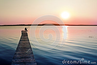 Colorful sunset over the lake with a pier. A lone fisherman is fishing on the pier. Stock Photo