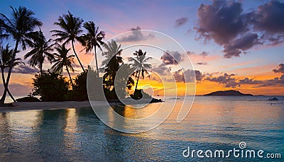 Colorful sunset over tranquil tropical island with silhouetted palm trees Stock Photo