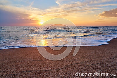 Colorful sunset at the tropical beach, sun behind clouds reflects on water. Stock Photo