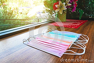 Colorful of surgical masks for Coronavirus Covid-19 protection on wooden table with artificial bouquet in the background. Stock Photo
