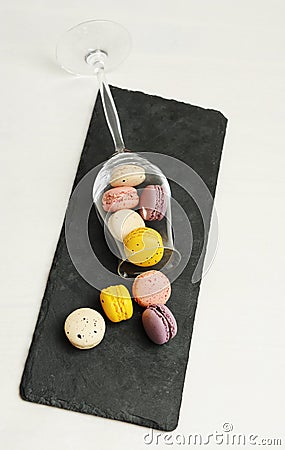 Colorful french mini macarons sprinkled from an overturned wine glass on slate board. White background Stock Photo