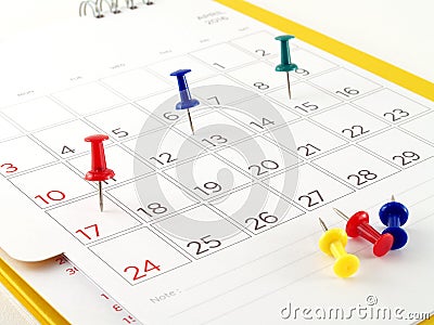 colorful thumbtacks tack on date in opened desk calendar page Stock Photo