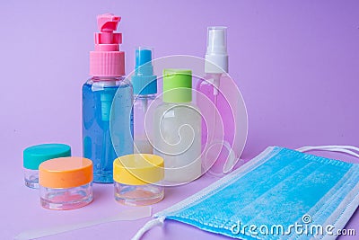 Colorful travel size bottles and medical masks on lavender background. Stock Photo