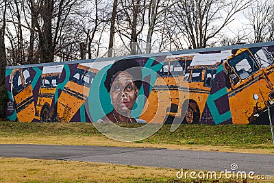 A colorful wall mural of an African American woman and a yellow school buss surrounded by yellow winter grass Editorial Stock Photo