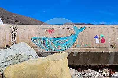 A colorful wall mural of a whale on the side of a highway at the beach surrounded by rocks with blue sky at Rincon Beach Editorial Stock Photo