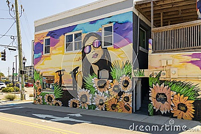 A colorful wall mural with a woman wearing sunglass, surfers at the beach and colorful flowers on the side of a building Editorial Stock Photo