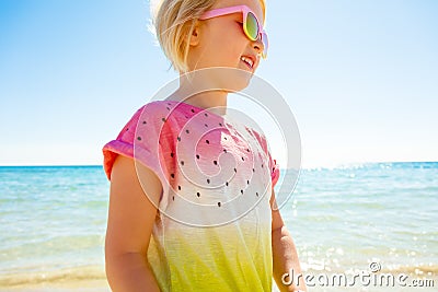 Smiling trendy girl in colorful shirt on seashore looking aside Stock Photo