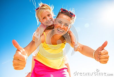 Smiling trendy mother and child on beach showing thumbs up Stock Photo