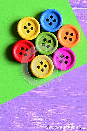 Colorful wooden round buttons laid out in the shape of a flower on a green paper sheet. Wooden background with copy space for text Stock Photo