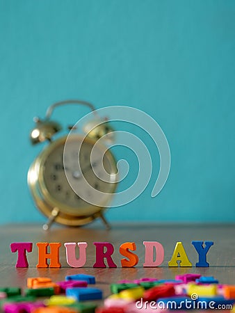 Colorful wooden word THURSDAY on wooden table and vintage alarm clock and background is powder blue. English alphabet made of wood Stock Photo