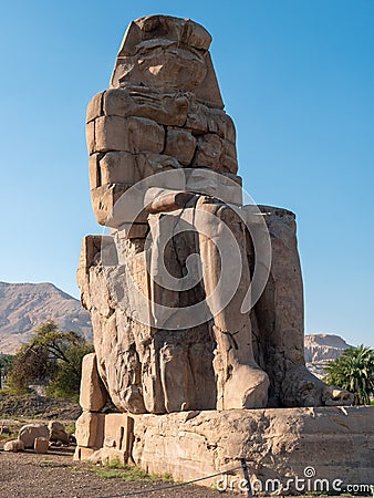 Colossi of Memnon - statues of Pharaoh Amenhotep III. Tall stone statue against the blue sky. Luxor, Egypt. Vertical Stock Photo
