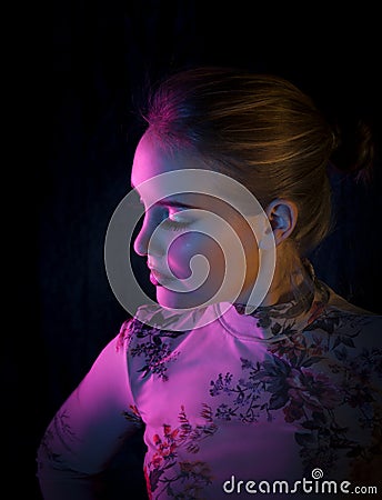 Colour portrait of beautiful blonde woman posing in creative colourful light of pink, orange and blue. Stock Photo