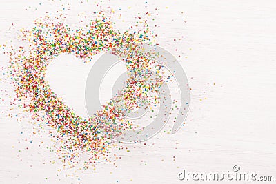 Colorful sprinkles sprinkled in shape of heart flatlay on white and grey wooden background Stock Photo