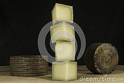 Column of pieces of semi-hard cheese and two Manchego cheeses in background Stock Photo