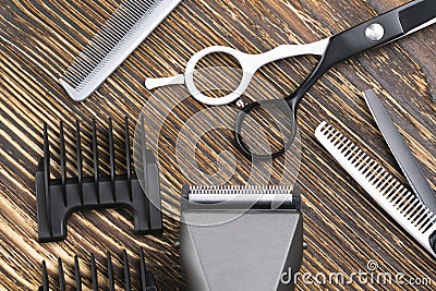 Comb, scissors, razor and hair clipper lie on a brown wooden table Stock Photo