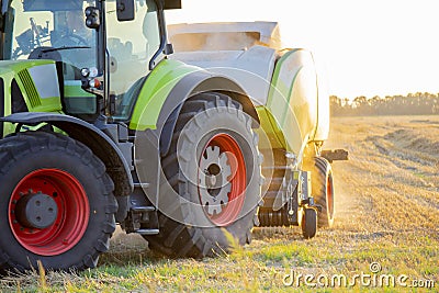 Combine harvester pressing straw from field into bales. Sunny summer evening Stock Photo